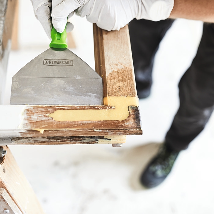 Ein Repair Care Anwender spachtelt eine mit Holzreparaturmasse gefüllte Reparaturstelle ab.