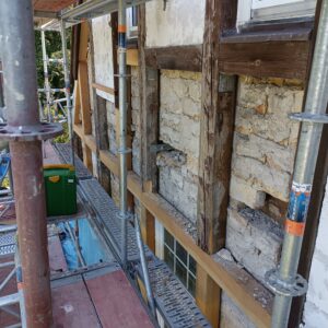 Deutliche Holzschäden an einem Fachwerkhaus: Rissbildung, Abplatzungen und Verwitterung an tragenden Holzbalken weisen auf fortgeschrittenen Verfall und Sanierungsbedarf hin.